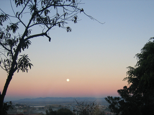 A full moon sets in the west amid the reflected glow of the sunrise.